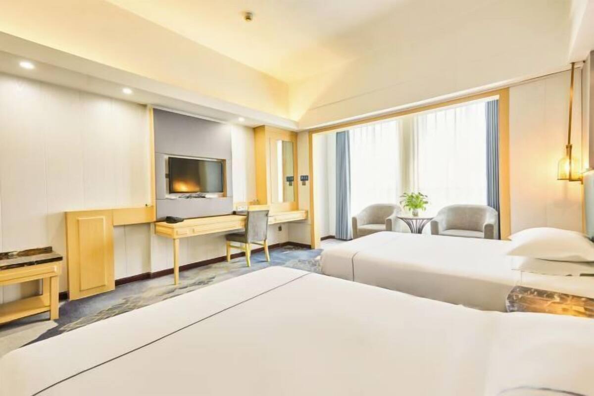 A hotel room with two beds, a desk, a TV, and a small seating area.
