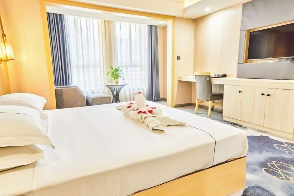A hotel room with a bed, a desk, a chair, a television, and a window with curtains.