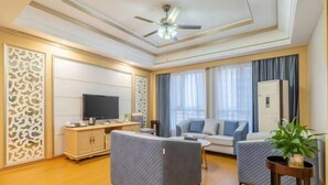 A modern living room with a flat-screen TV, a sofa, a coffee table, and a ceiling fan. - Magnotel Hotel (Yichang CBD Shopping Center) (Yichang)