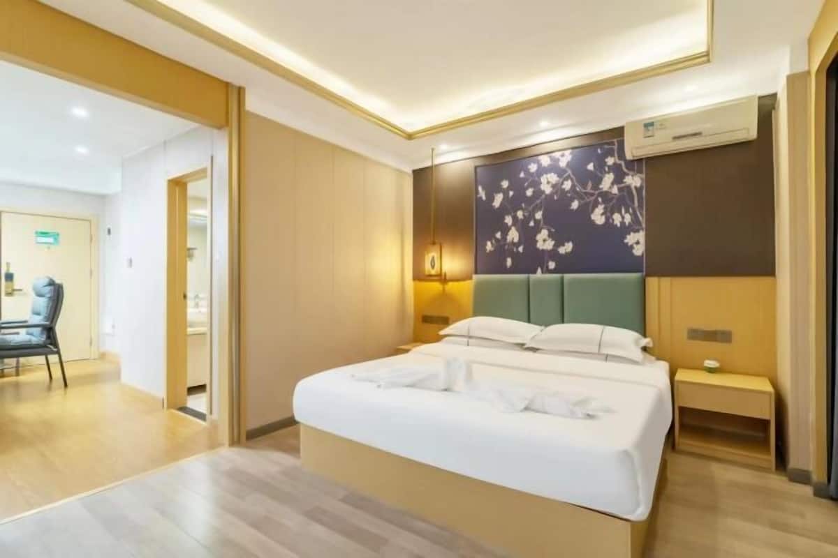 A hotel room with a bed, bedside table, lamp, and a wall with a floral design.