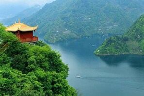 A traditional building with a red roof and a golden eave, overlooking a calm lake surrounded by lush green hills. - Yulan Hotel (Yichang CBD Shopping Center) (Yichang)