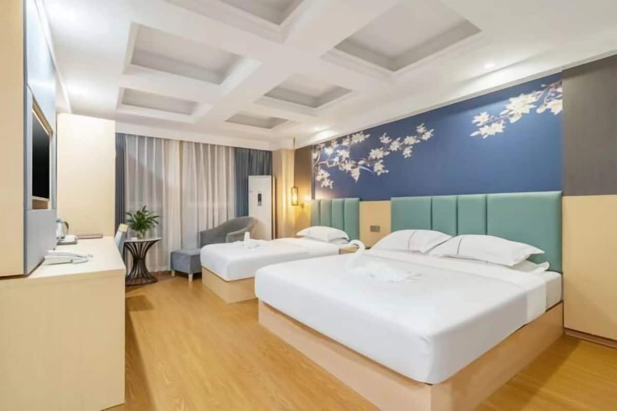 A hotel room with two beds, a desk, a chair, and a small table with a plant.