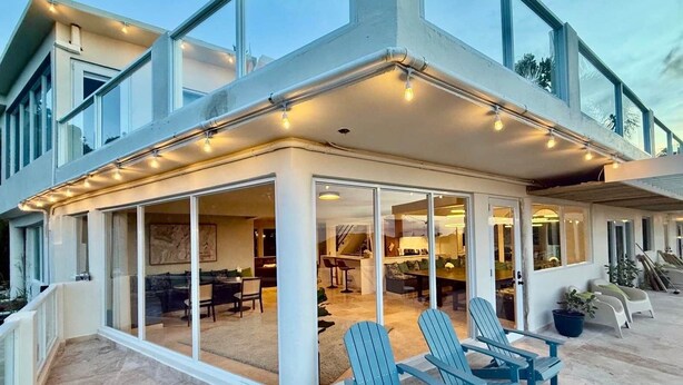 Ein modernes Haus mit überdachter Terrasse, Schiebetüren, Sitzgelegenheit im Freien und Blick ins Innere.
