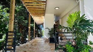 Eine Steintreppe führt zu einer Holzpergola mit Pflanzen, umgeben von Grün und einem Gebäude mit weißer Fassade.
