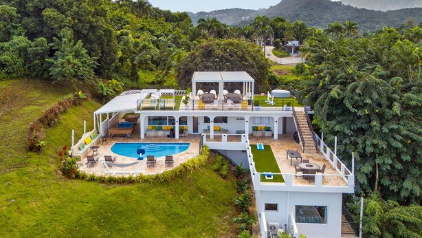 Ein modernes Haus mit Pool, Sitzgelegenheiten im Freien und Blick auf die umliegende Grünfläche und Hügellandschaft.