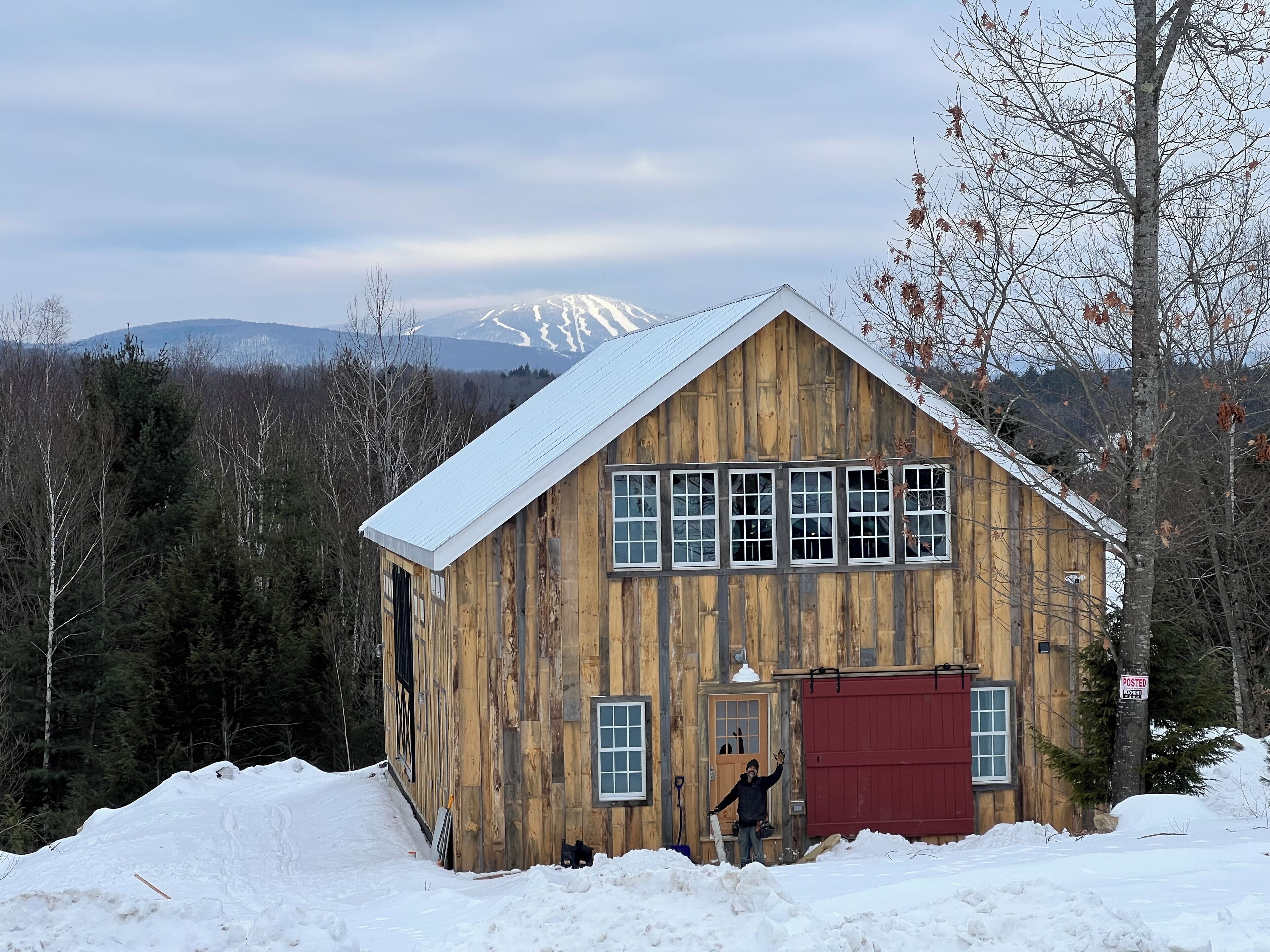 Eine Holzhütte mit roter Tür, umgeben von Schnee und Bäumen, mit einem Berg im Hintergrund.