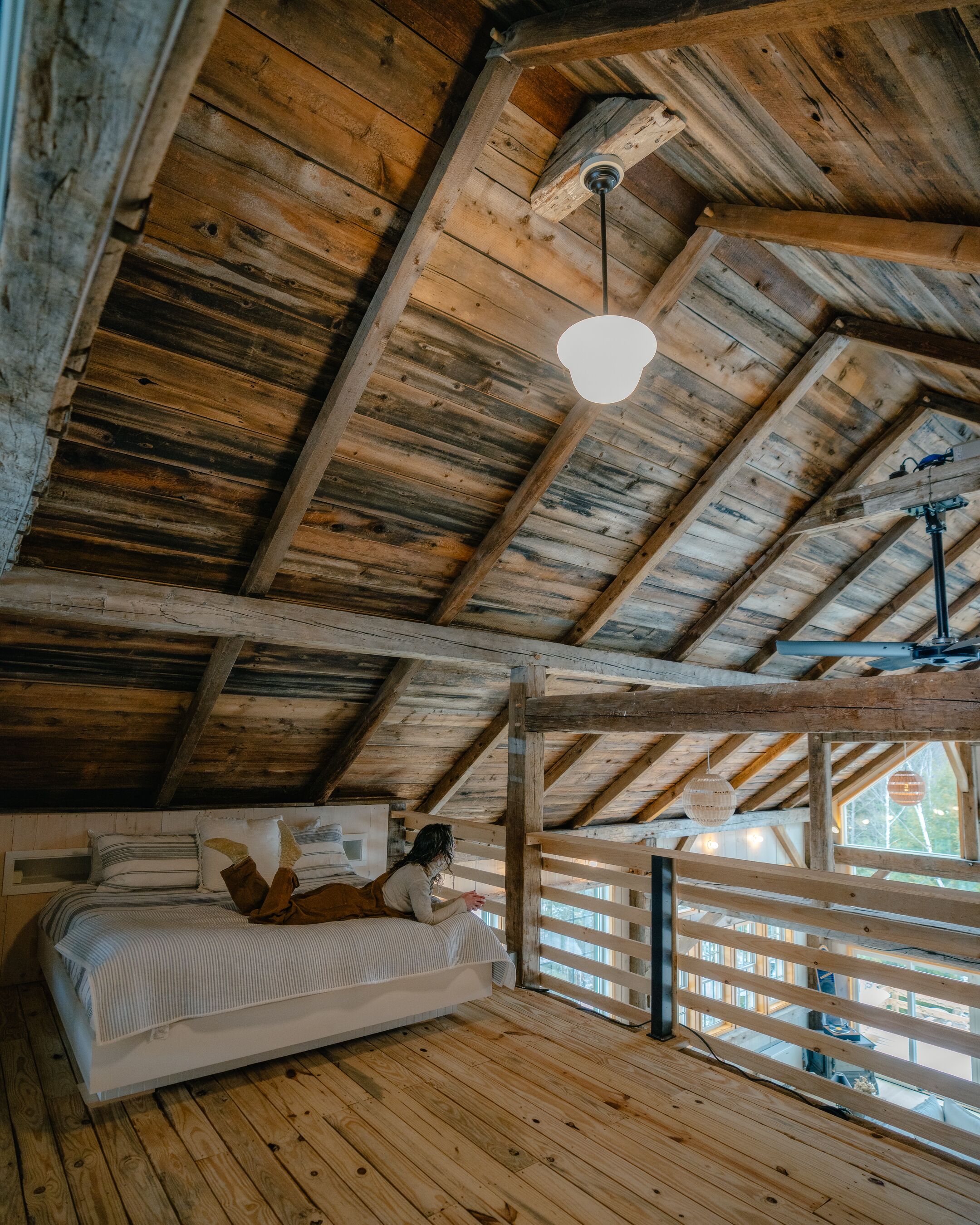 Une pièce rustique en bois, dotée d’un lit en mezzanine, d’un luminaire suspendu et d’une fenêtre donnant sur l’extérieur.