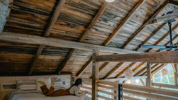 Una habitación rústica de madera con cama elevadas, una lámpara colgante y una ventana con vistas al exterior.