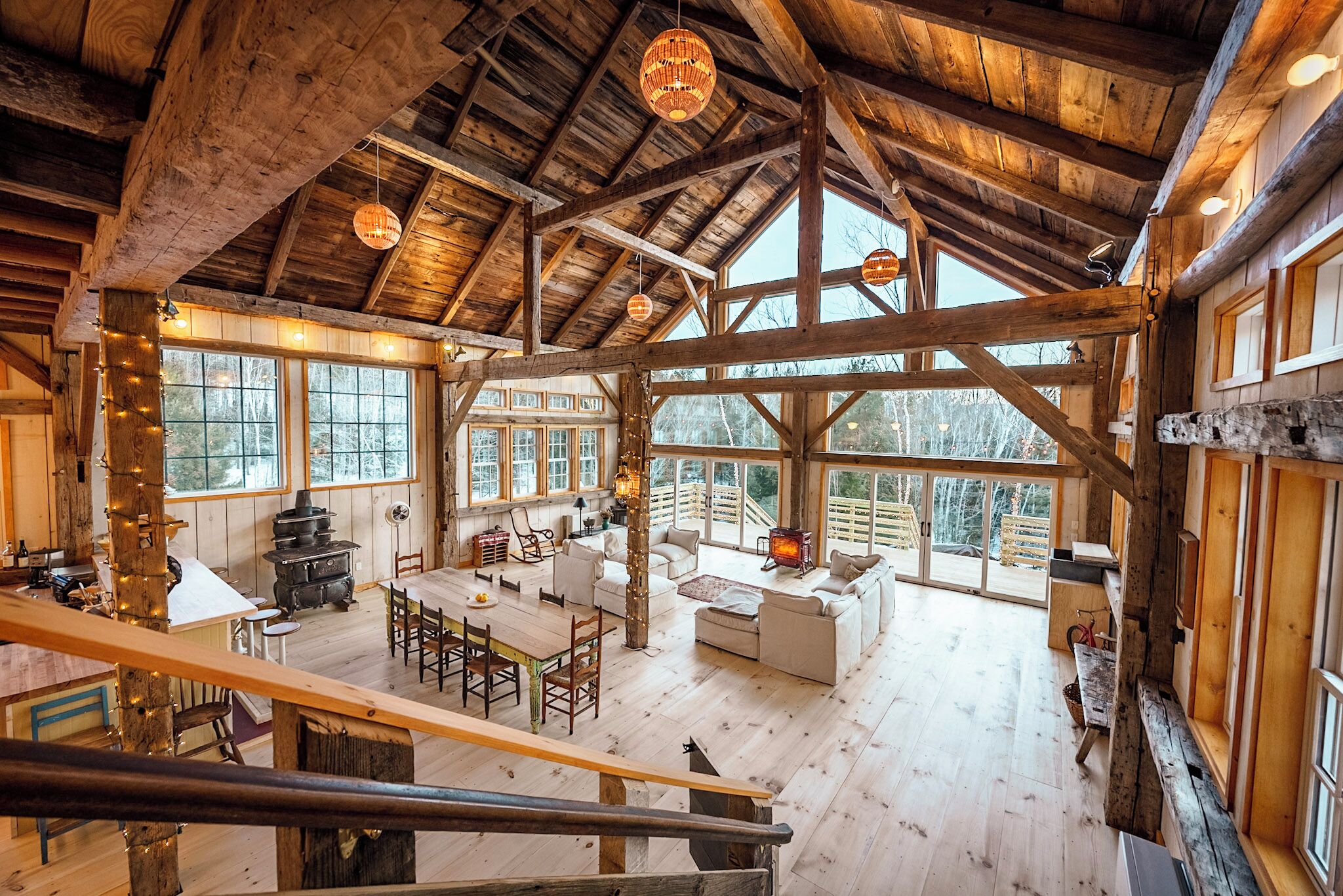 A spacious wooden cabin with a high ceiling, large windows, a dining area, and a cozy living room.