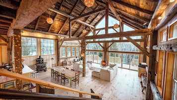 A spacious wooden cabin with a high ceiling, large windows, a dining area, and a cozy living room.