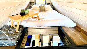 A small, cozy room with a sloped ceiling, a bed with white bedding, a small table with a plant, and a window with a view of trees. - A FRAME ALPHA -WoW This Old Tree
 (Five Islands)