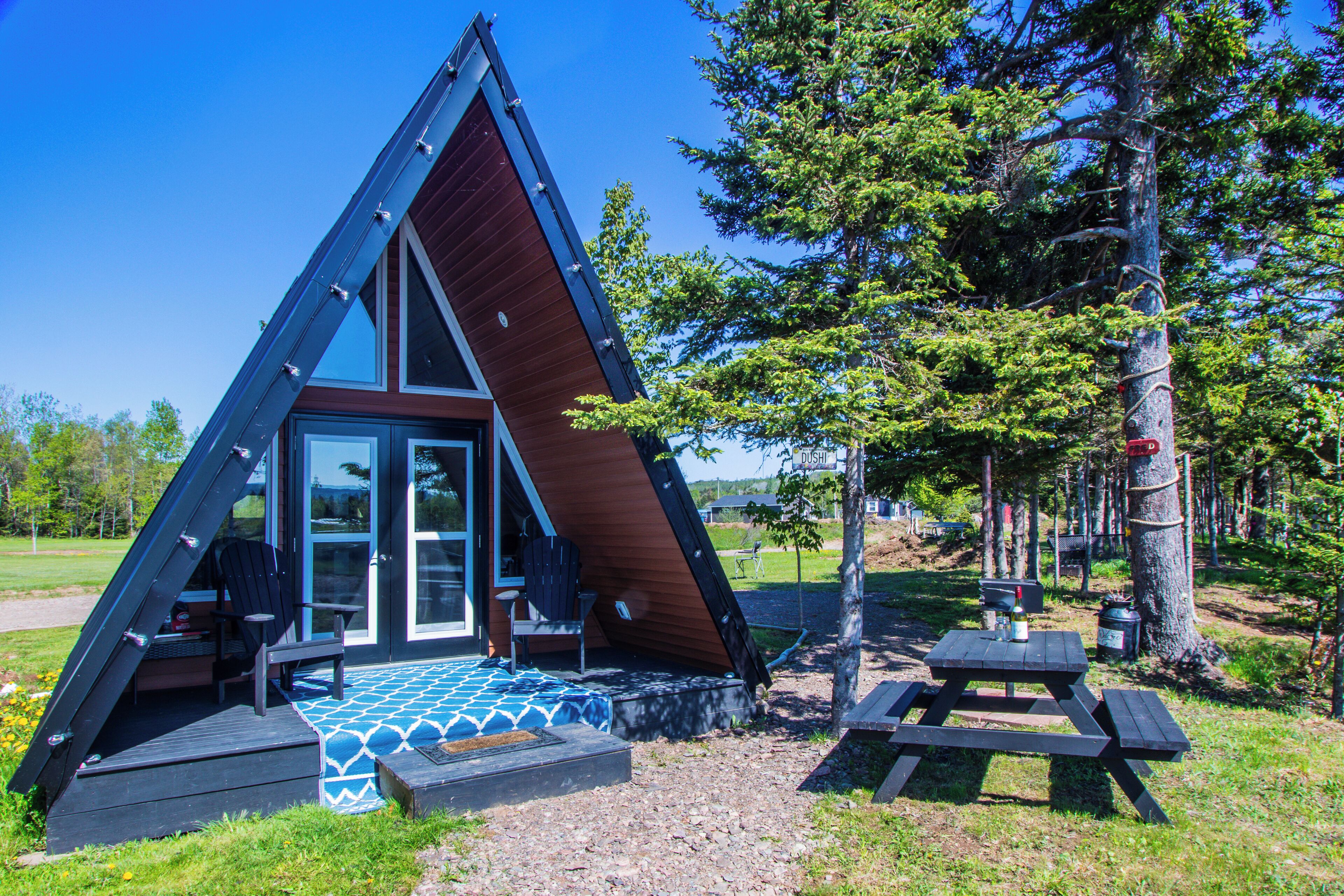 A triangular cabin with a glass door entrance, a small porch, and a picnic table nearby.
