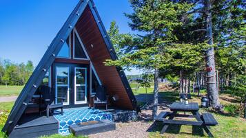 A triangular cabin with a glass door entrance, a small porch, and a picnic table nearby.