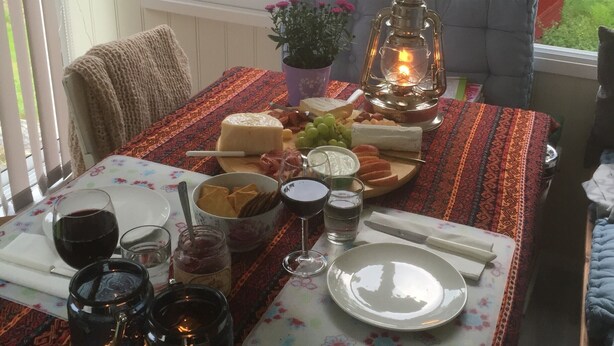 Ruokapöytä on katettu erilaisilla ruoilla ja juomilla, siinä on lyhty, ja ikkunasta avautuu näkymä taloon.