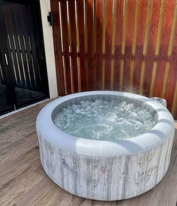 A round hot tub with a wooden exterior, labeled 'SALUSPA,' placed outdoors on a wooden deck.