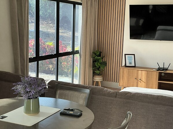 A room with a sofa, a small table with a vase, a potted plant, a wooden cabinet, and a TV mounted on the wall.