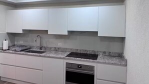Cozinha moderna com armários brancos, bancada de granito, lava-louças embutida e pia de aço inoxidável.