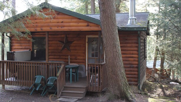 Une cabane en rondins avec une véranda, deux chaises et une décoration en forme d’étoile.