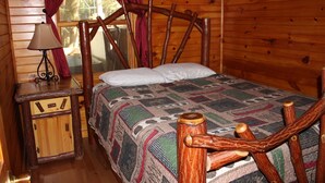 Une chambre à coucher dans une cabane en bois, avec un lit, une table de chevet, une lampe et une fenêtre avec des rideaux.
