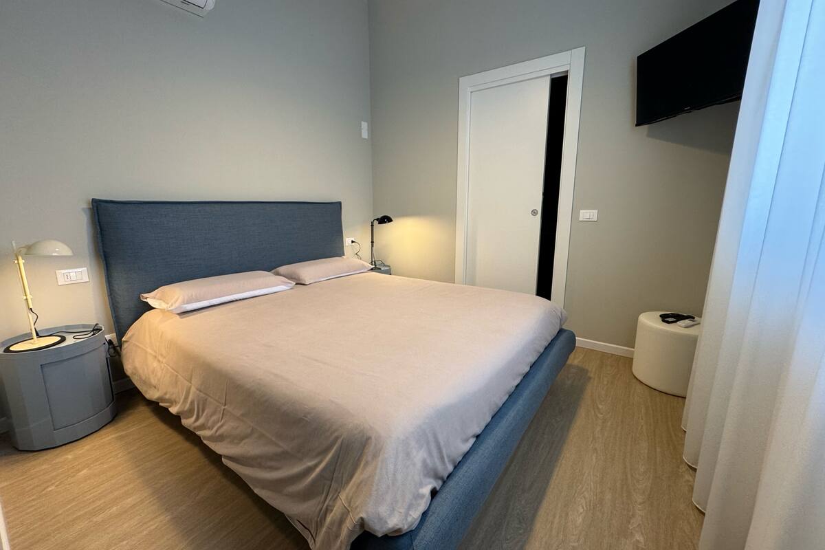 A neatly made bed with a headboard, a bedside table with a lamp, and a wall-mounted TV.