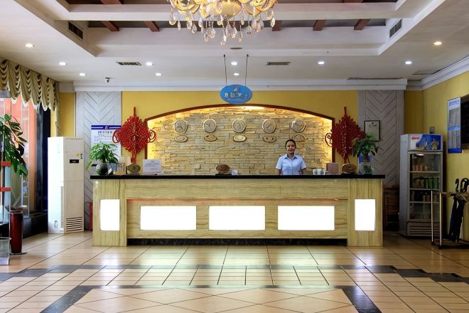 A hotel reception desk with a receptionist, a clock, and a decorative wall.