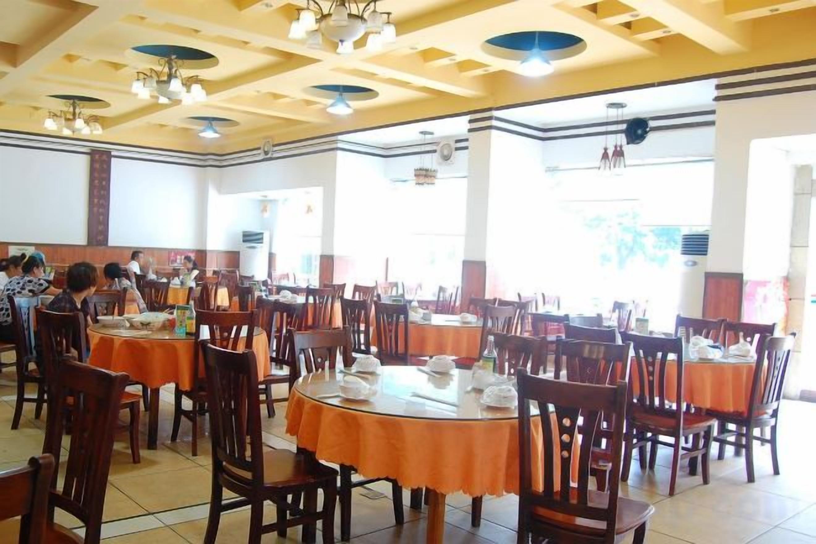 A dining area with multiple tables and chairs, a high ceiling with exposed beams, and large windows allowing natural light.