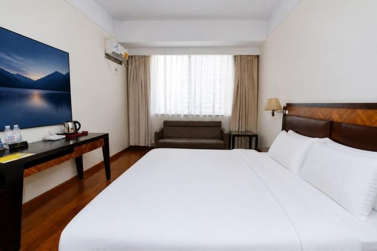 Habitació d'hotel amb un llit gran, una taula de treball amb una cadira, un televisor i una finestra amb cortines.