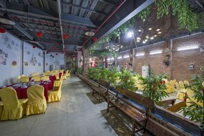 Un restaurant avec des chaises jaunes, un mur en briques et des plantes suspendues.