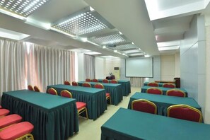 Une salle de conférence équipée de tables et de chaises, d’un écran de projection et d’un tableau blanc.