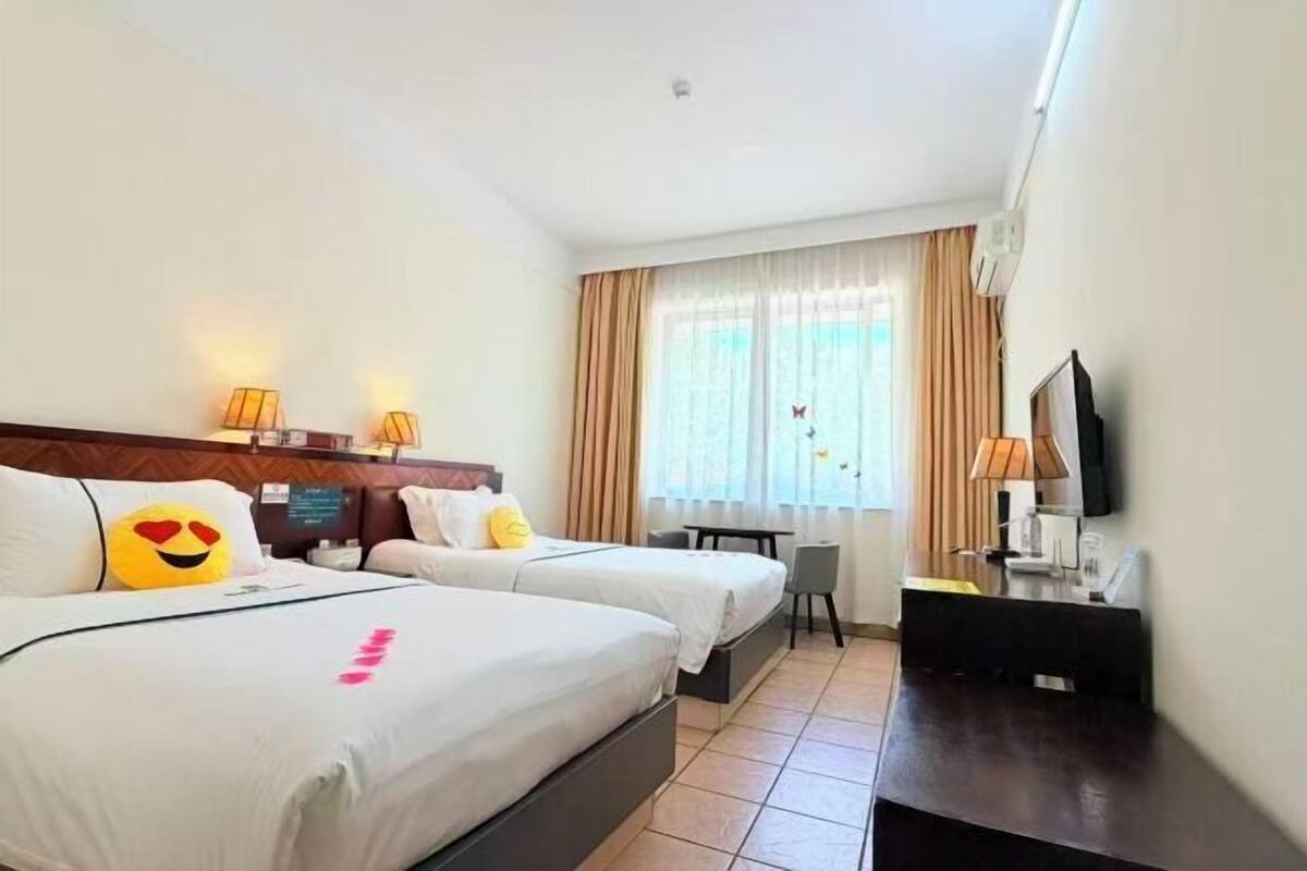 Ein Hotelzimmer mit zwei Betten, einem Schreibtisch, einem Sessel, einem Fernseher und einem Fenster mit Vorhängen.