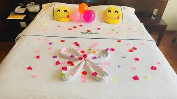 A hotel room with a neatly made bed, pillows with smiley faces, and a bouquet of flowers on the bed.