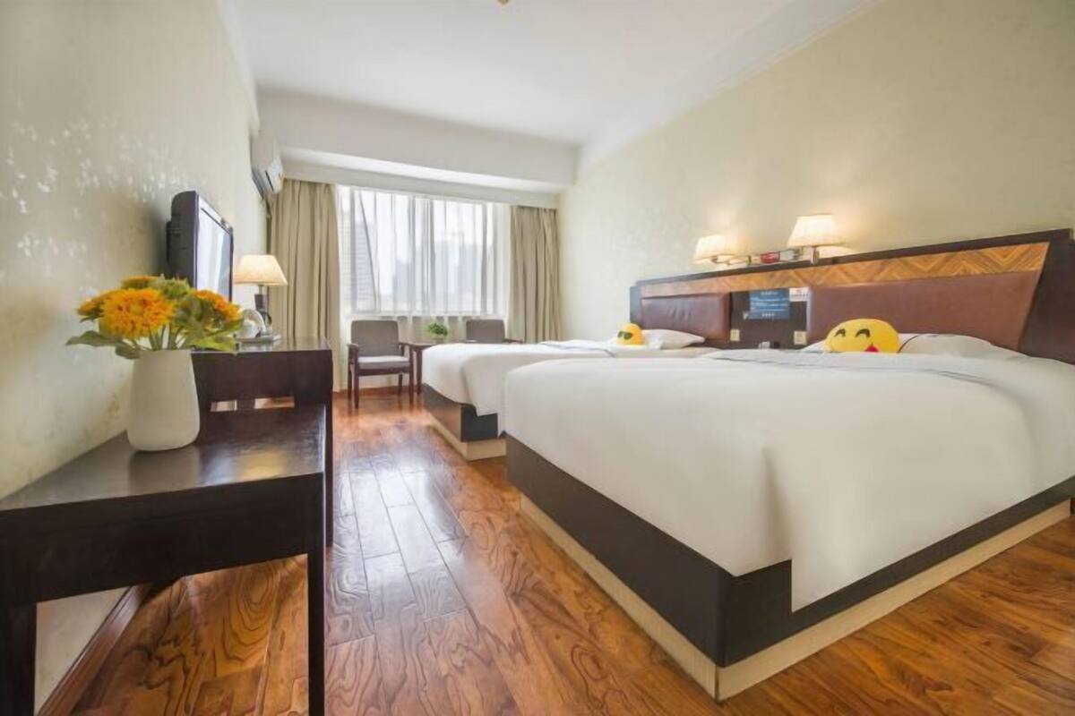 Ein Hotelzimmer mit einem großen Bett, einem Schreibtisch, einem Stuhl, einem Fernseher und einem Fenster mit Vorhängen.