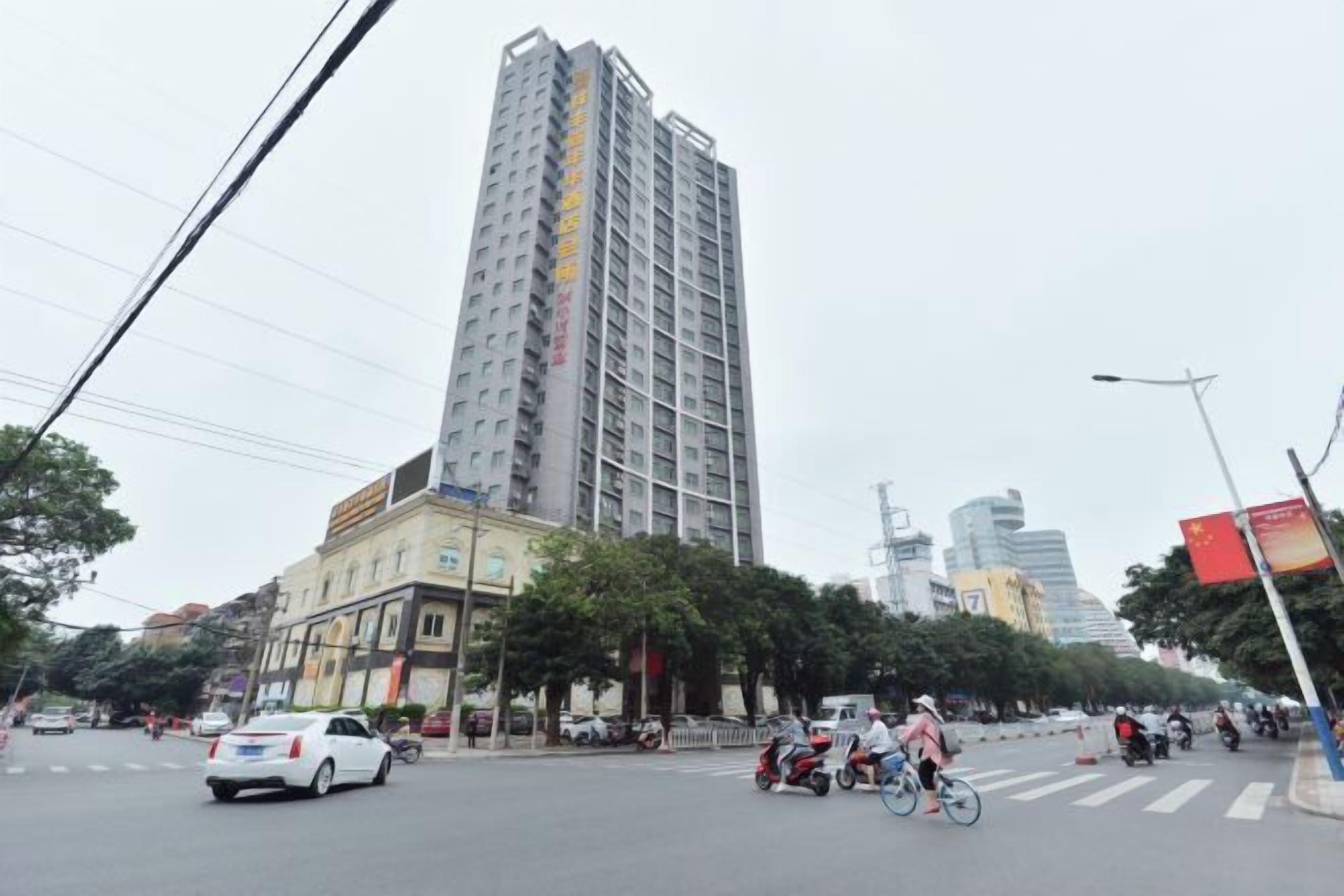 Um edifício com vários andares e design arquitetônico moderno, situado em ambiente urbano com uma rua movimentada e outros edifícios altos ao fundo.