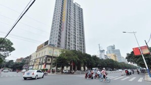Un edifici de diverses plantes amb un disseny arquitectònic modern, situat en un entorn urbà amb un carrer animat i altres edificis alts al fons.