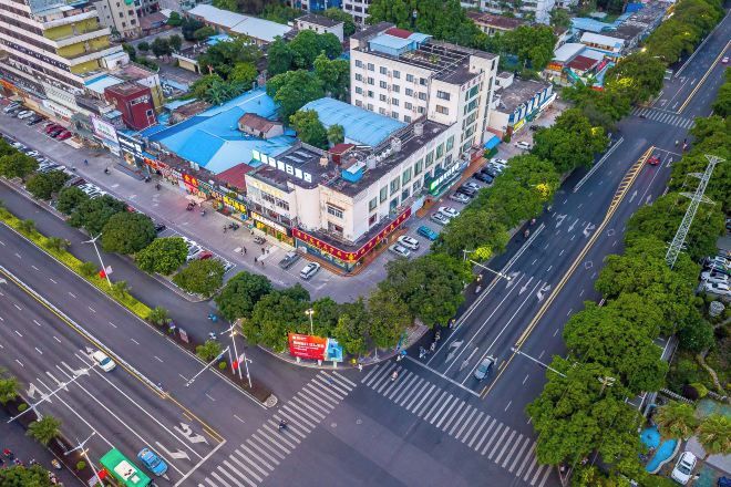 An aerial view of a city intersection with buildings, roads, and greenery.