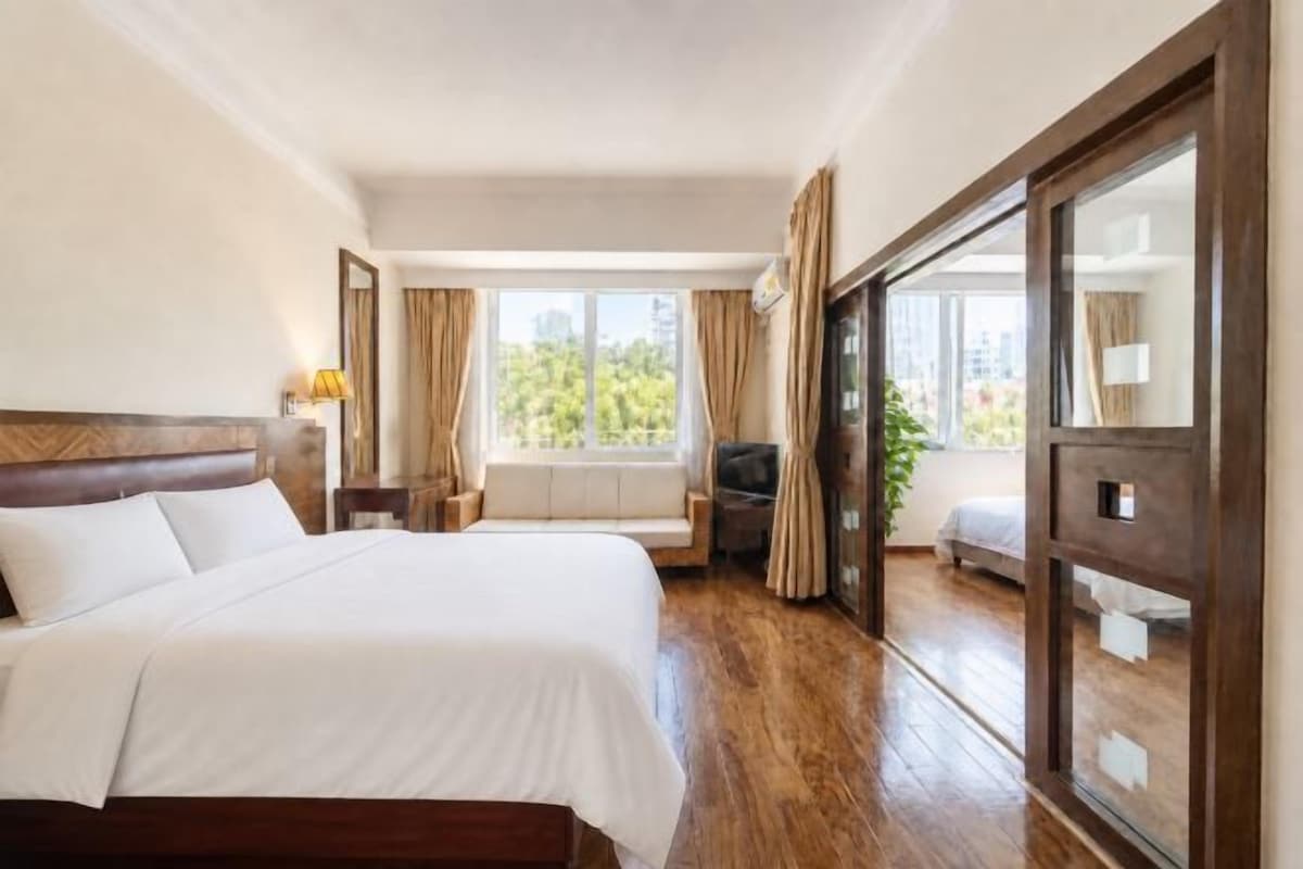 Habitació d'hotel amb un llit gran, una taula de treball, una cadira, una finestra amb cortines i una porta de vidre corredissa.