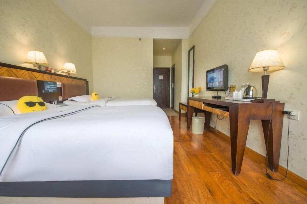 A hotel room with two beds, a desk, a television, and lamps.