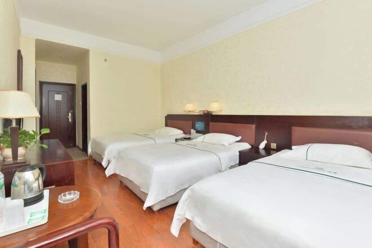 A hotel room with two beds, a desk with a lamp, and a small table with a kettle and a glass.