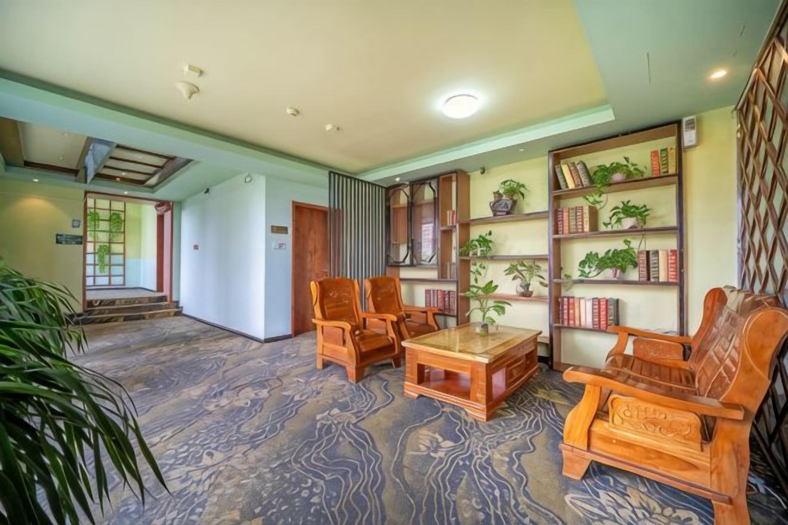 Un vaste espace de vie agrémenté d’une table basse en bois, de deux chaises en bois et d’une bibliothèque remplie de livres et de plantes.