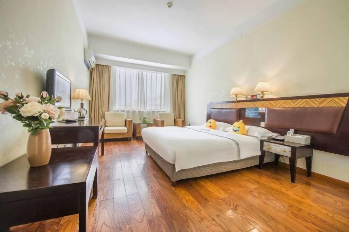 Ein Hotelzimmer mit Bett, Nachttischen, Schreibtisch, Stuhl, Fernseher und einem Fenster mit Vorhängen.