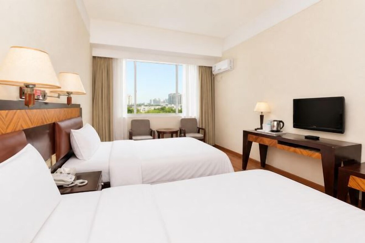 Habitació d'hotel amb dos llits, televisió, escriptori amb làmpada i vista a una ciutat.