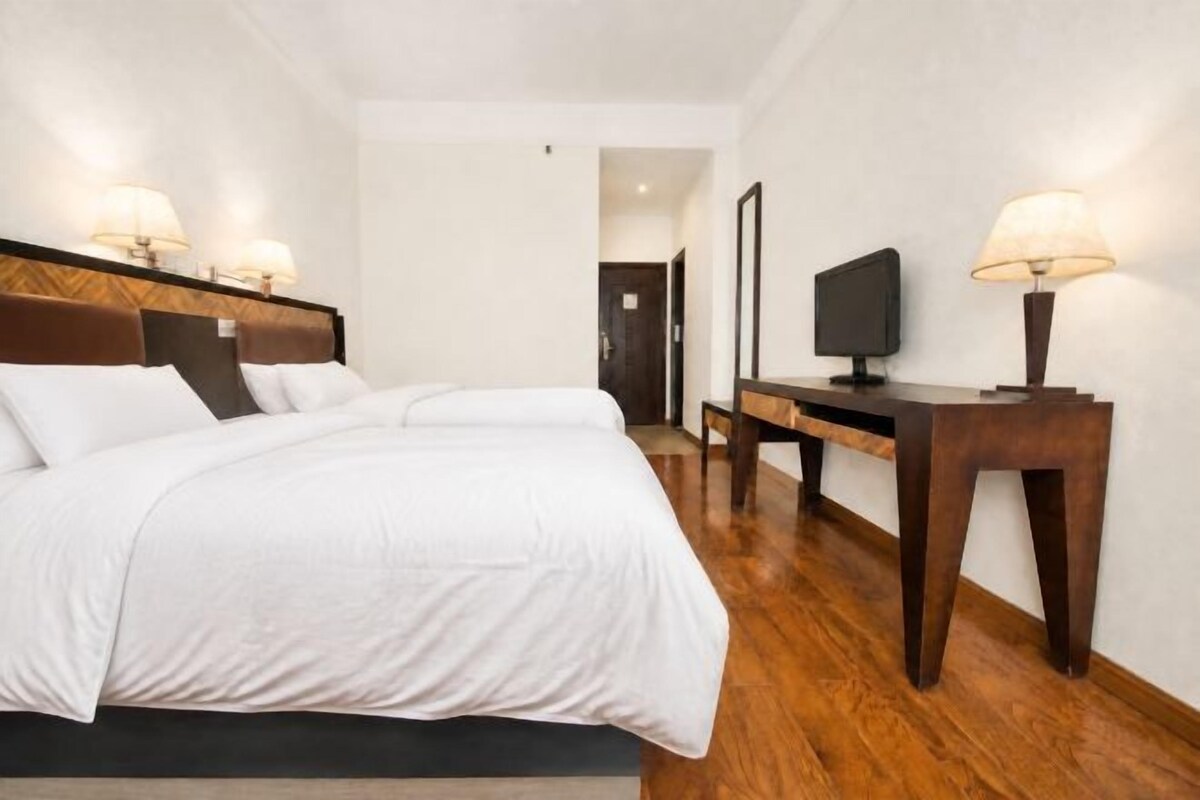 Habitació d'hotel amb un llit gran, aburnessors, un televisor de pantalla plana i una tauleta de nit de fusta.