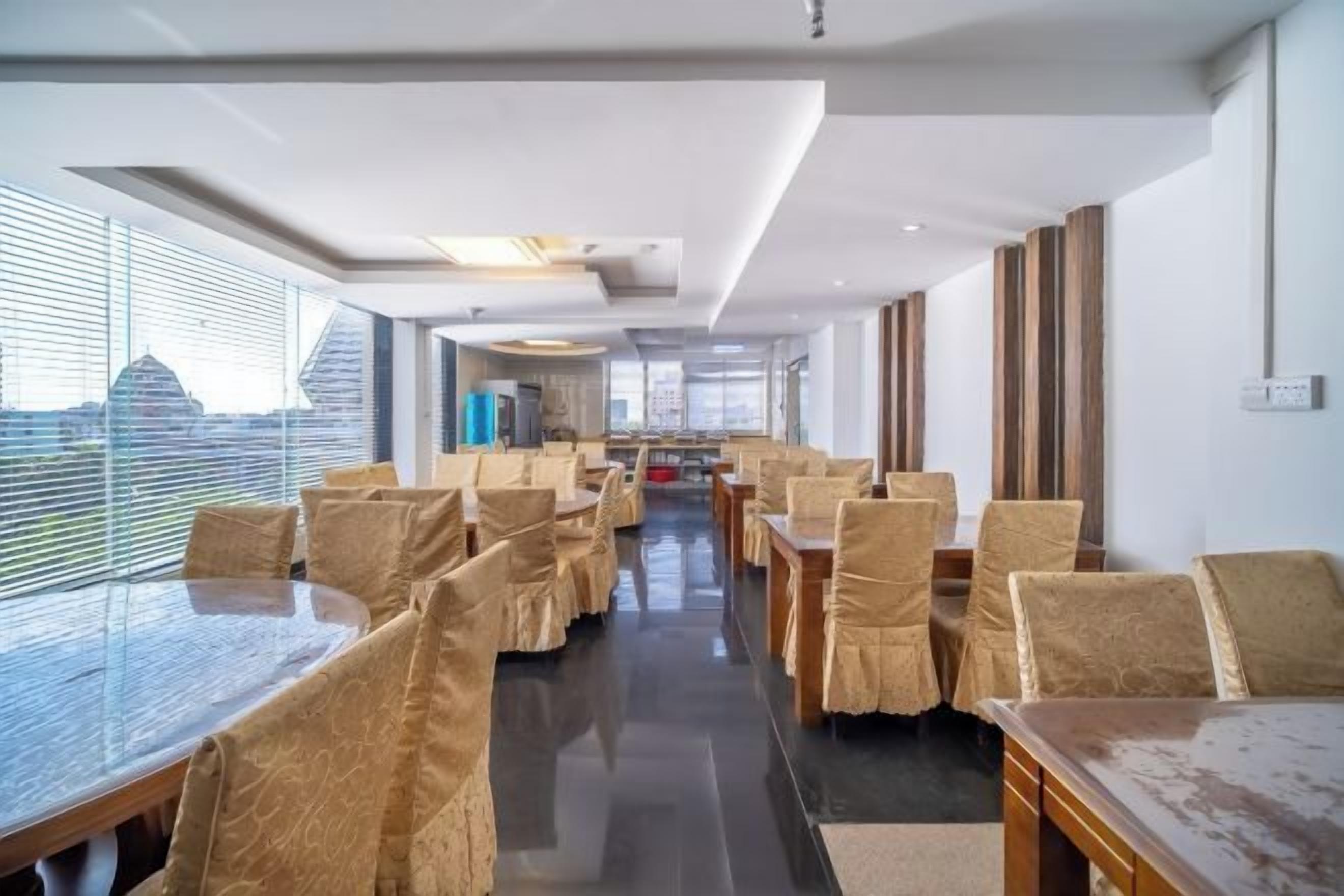 Un comedor de hotel con mesas y sillas, ventanas amplias y vistas a la ciudad.