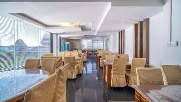 Un comedor de hotel con mesas y sillas, ventanas amplias y vistas a la ciudad.