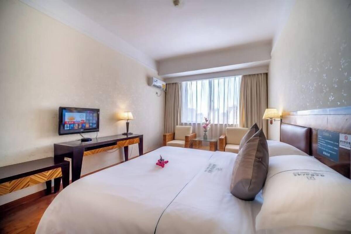 Ein Hotelzimmer mit einem großen Bett, einem Schreibtisch mit Computer, einem Fernseher und einem Fenster mit Vorhängen.