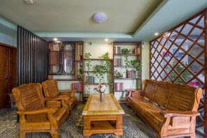 A room with a wooden sofa set, a coffee table, and a bookshelf with plants.