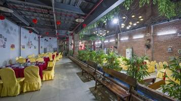 Un restaurante con mesas y sillas largas, una pared de ladrillo y plantas colgantes.