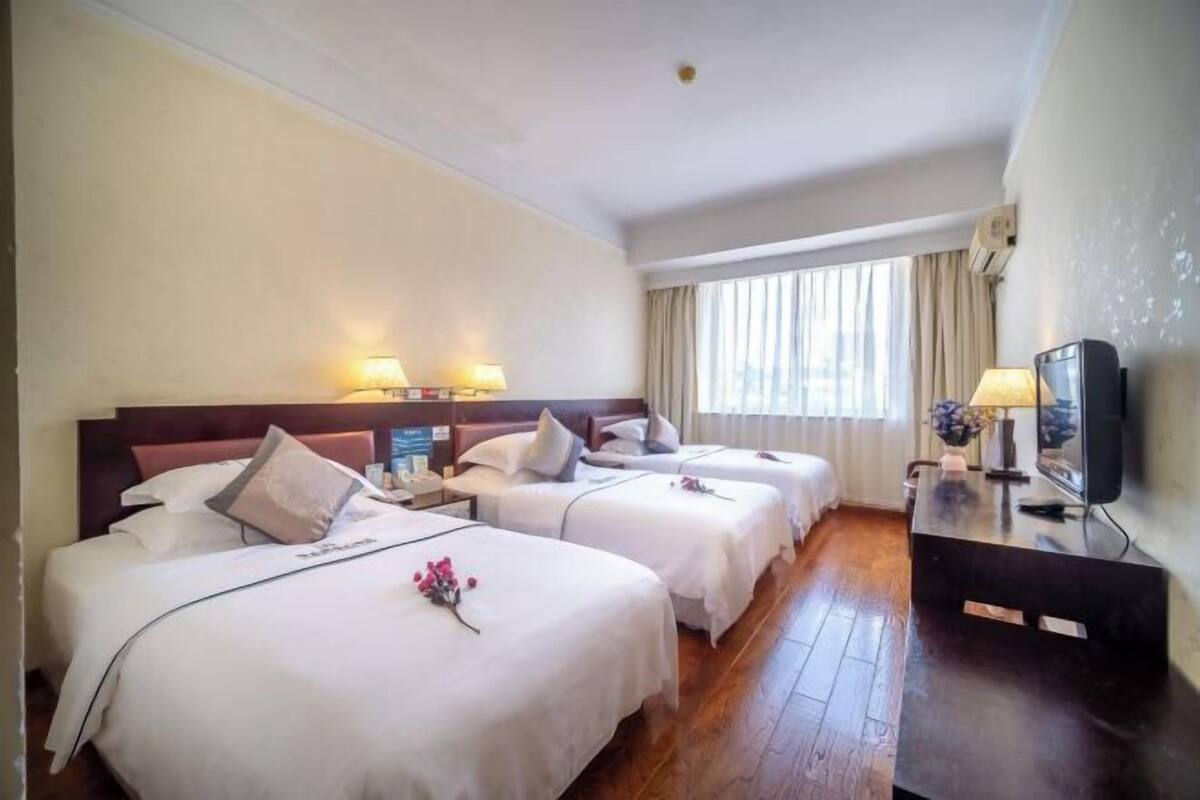 Ein Hotelzimmer mit drei Betten, einem Fernseher und einem Schreibtisch mit Lampe.