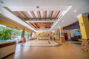 A hotel lobby with a reception desk, a large seating area, and a view of the outside.