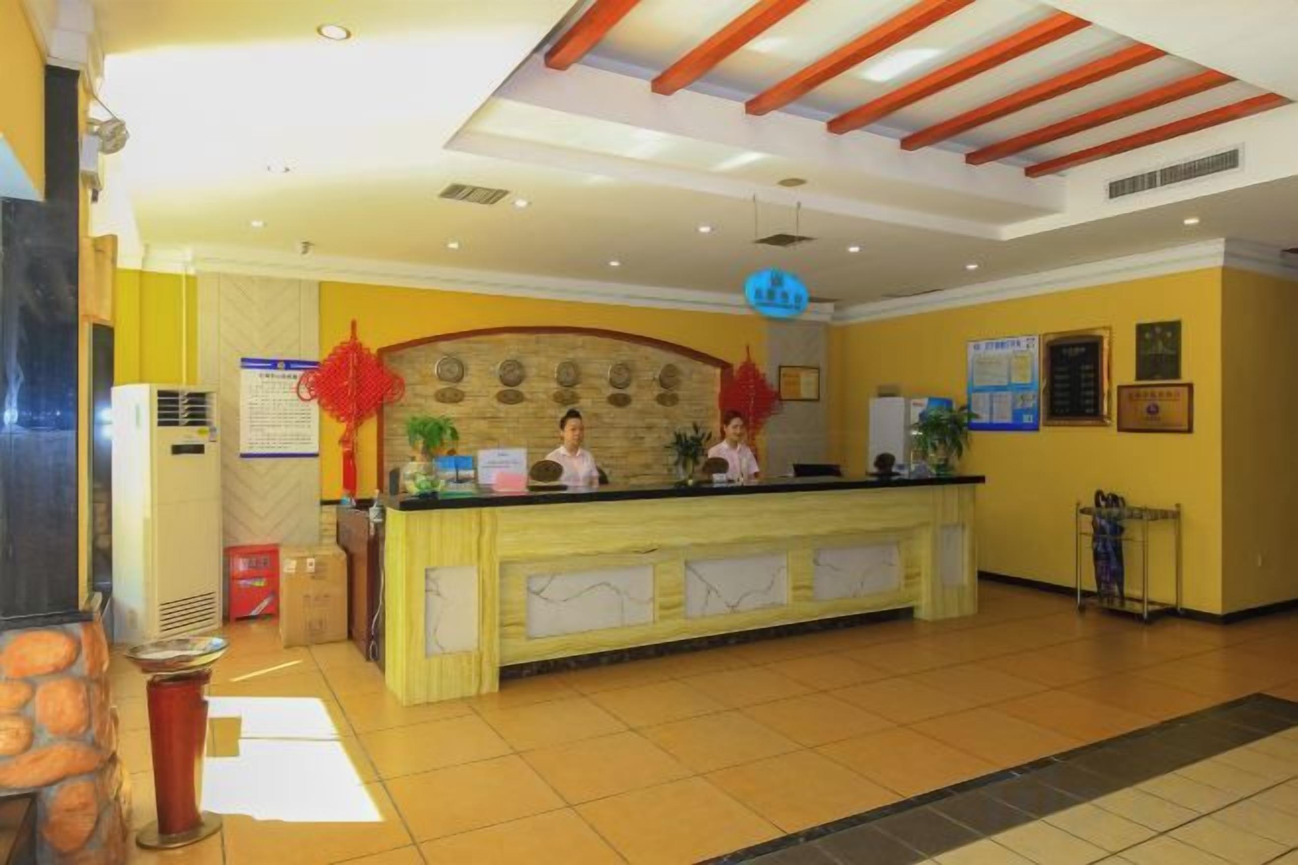Un'area reception di un hotel con una scrivania, due addetti alla reception, una decorazione a lanterna rossa e un soffitto con travi in legno.